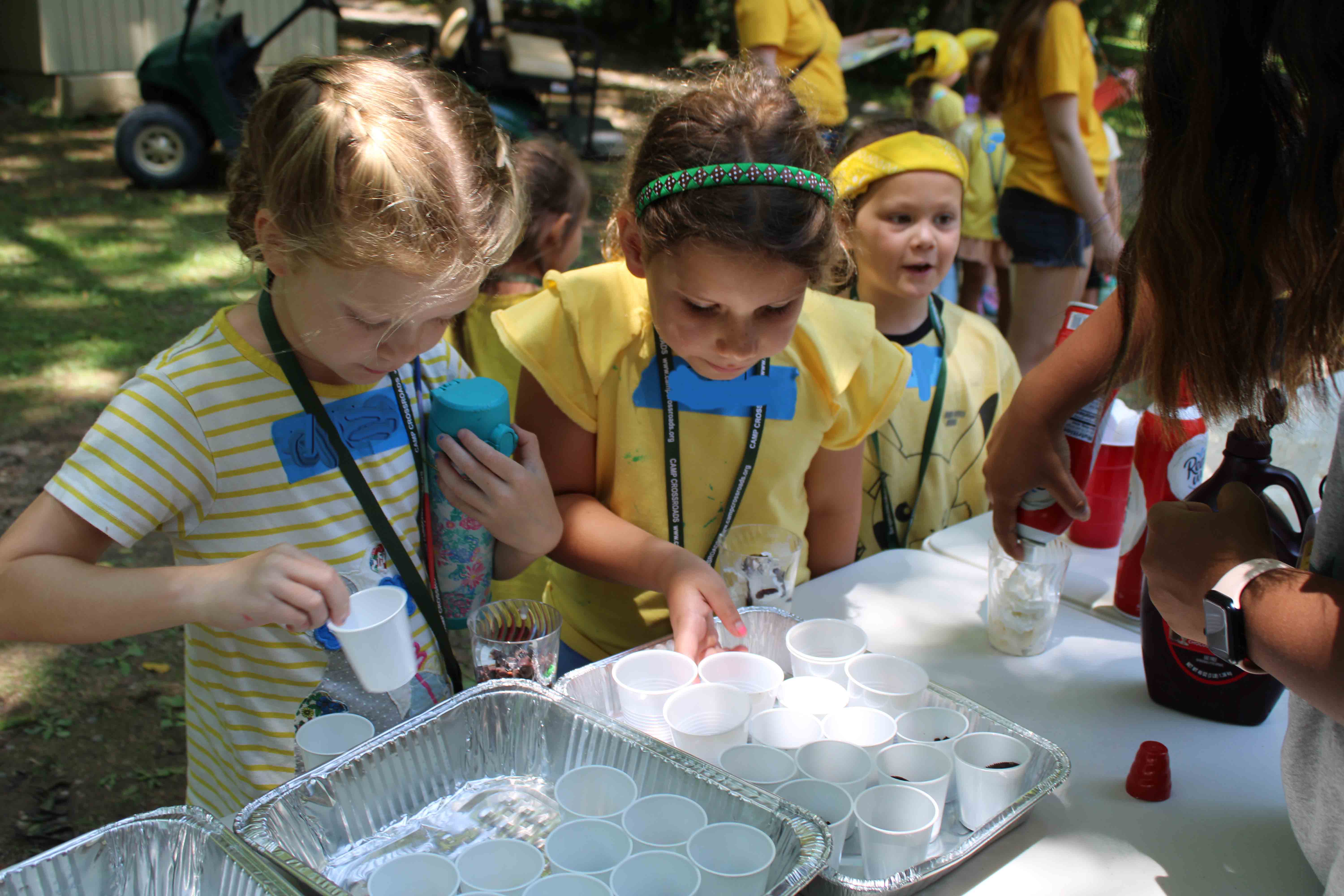 Campers from the Bats unit lining up outside to get cups of ice cream treats and toppings on a hot day.