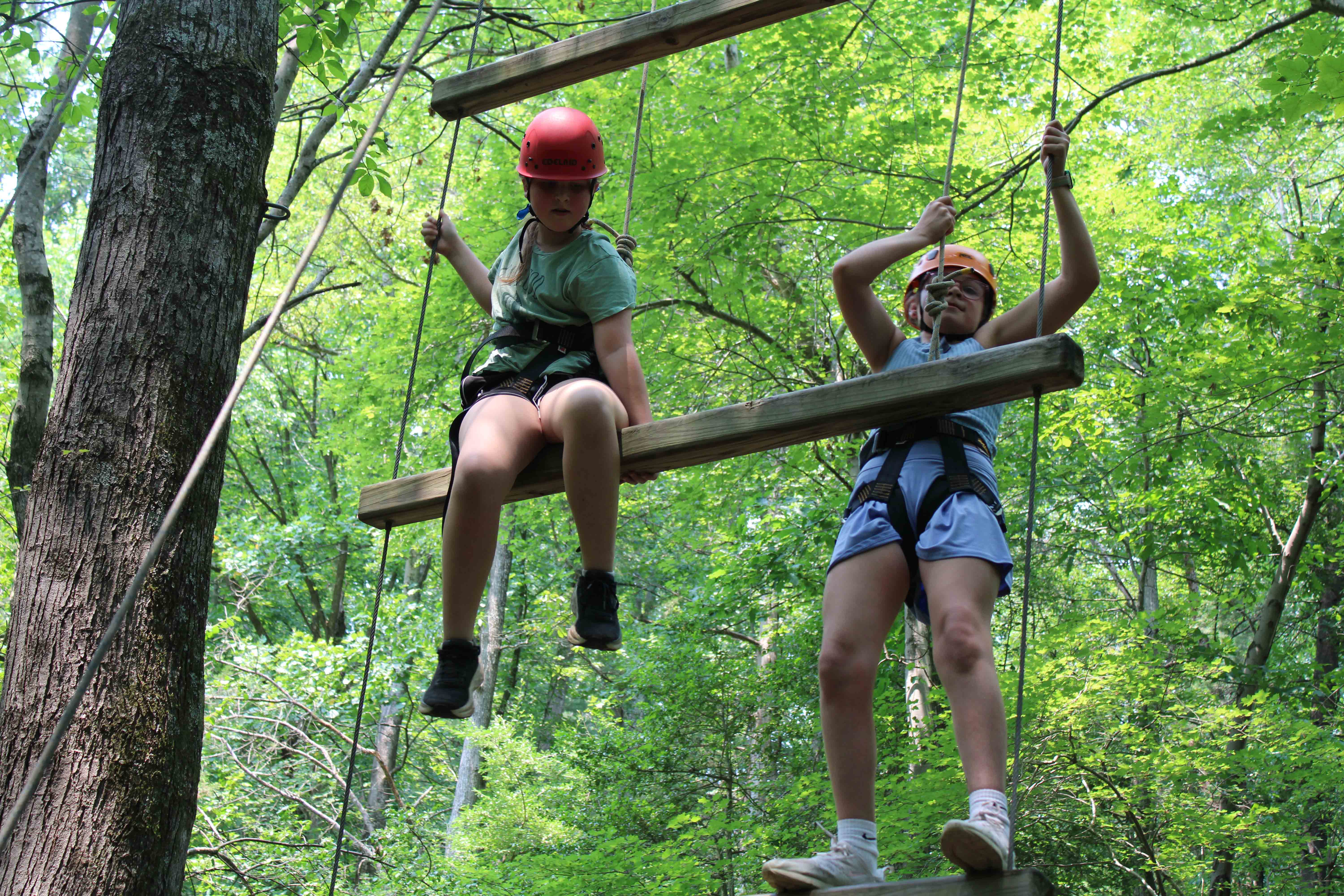 Campers traversing high up across a wooden log on the outdoor ropes course.