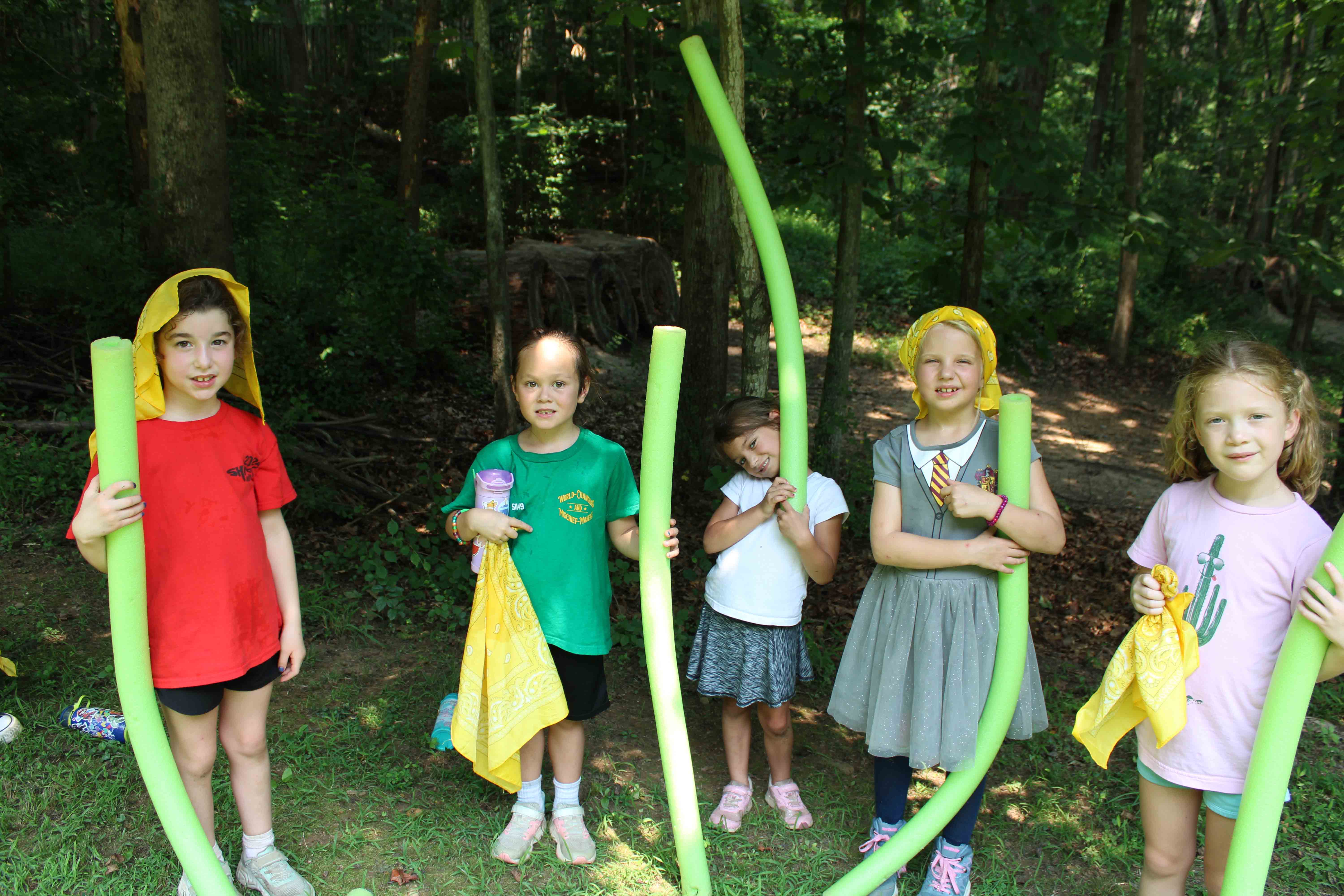 Campers playing with green pool noodles and water toys outside to cool off.