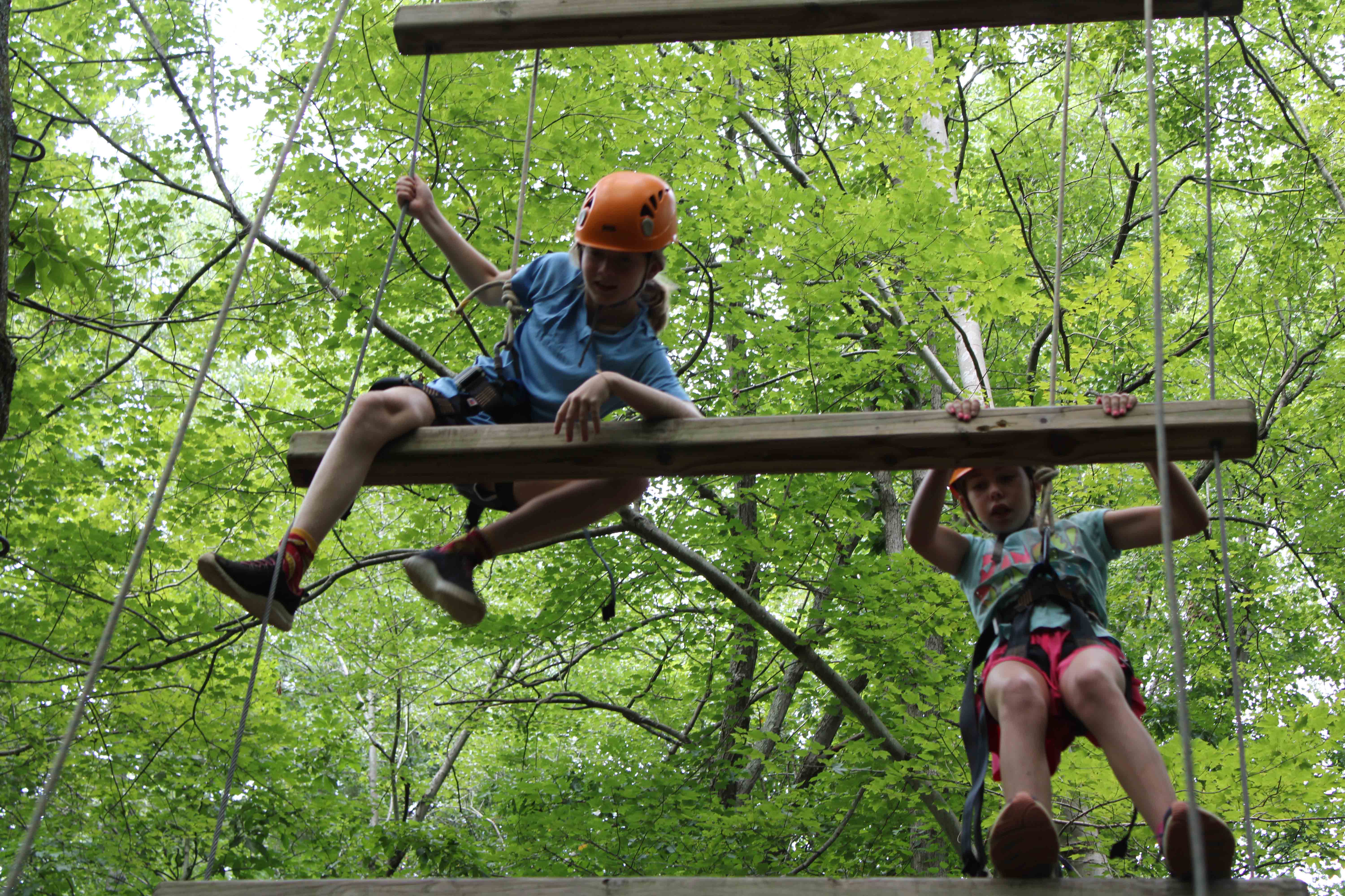 A brave camper perched high up in the trees on the challenge course zipline.
