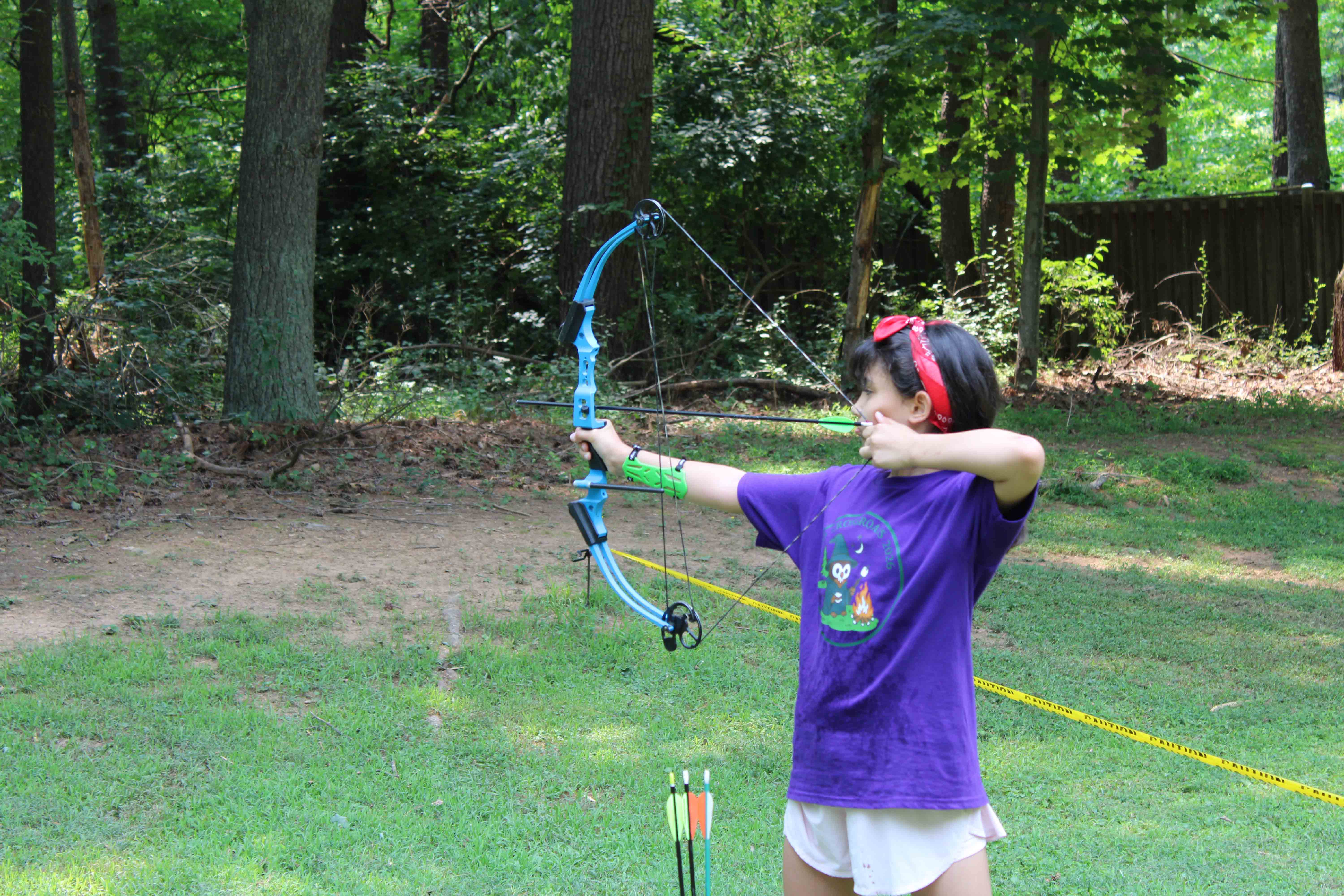 A close-up shot of a camper drawing back a red compound bow at the range.