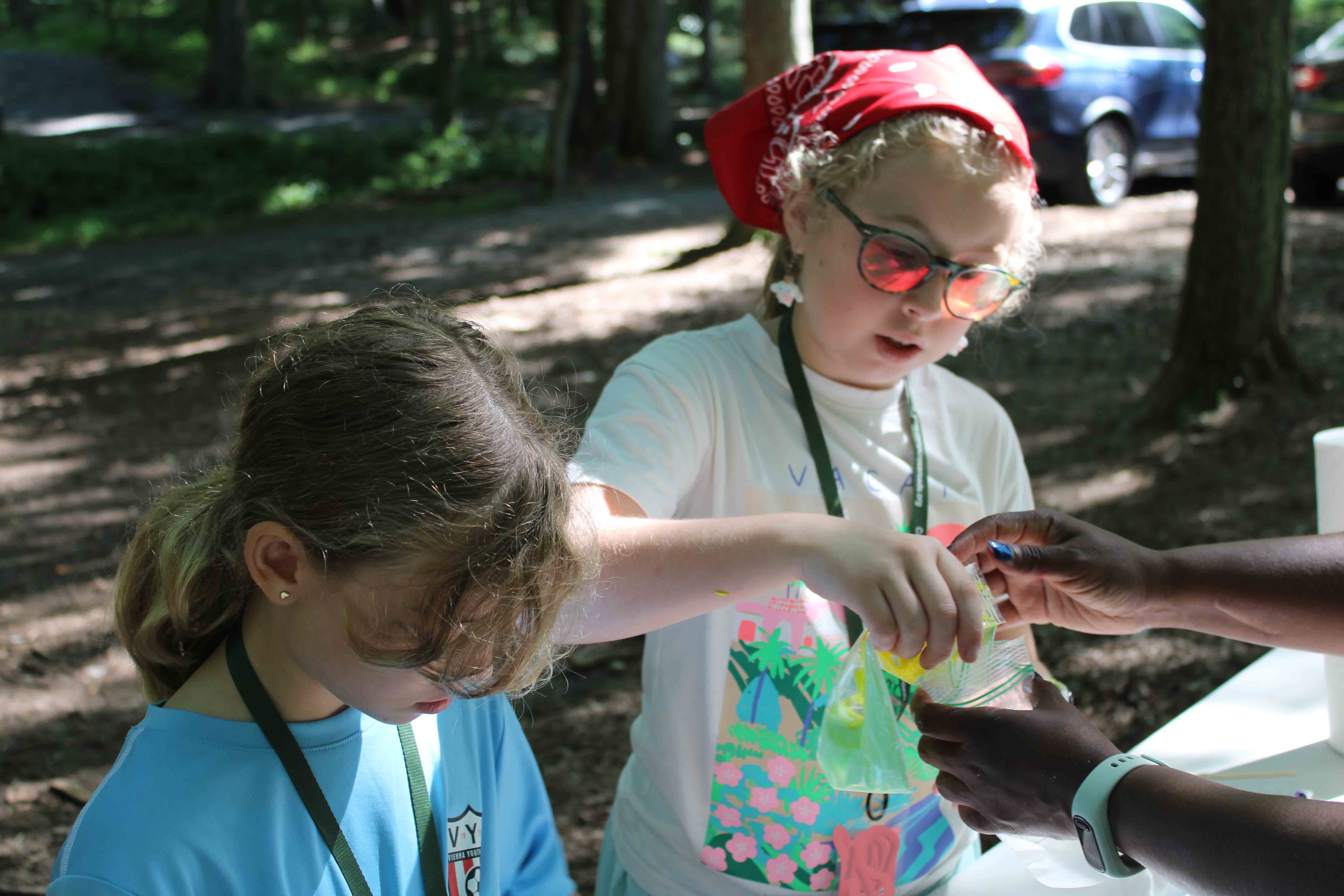 Campers conducting a colorful liquid science experiment under a shaded pavilion.